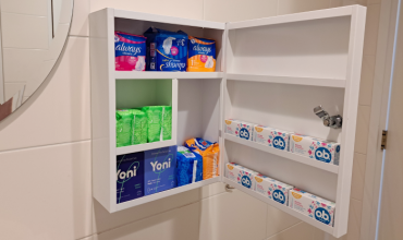 Een wit kastje met menstruatieproducten zoals maandverband en tampons hangt aan de muur.