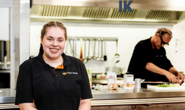 Renee, een jonge vrouw voor de balie van de keuken van de catering met een collega werkend op de achtergrond