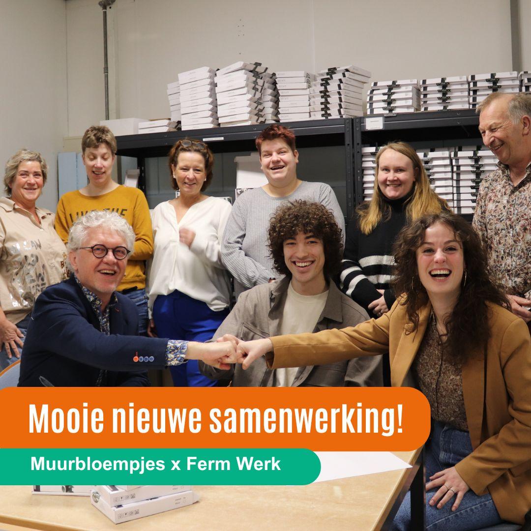 De oprichters van Muurbloempjes en directeur van Ferm Werk geven elkaar een boks boven het contract dat zij net hebben getekend. De medewerkers van Ferm Werk die de productie gaan doen en hun leidinggevenden staan er omheen.